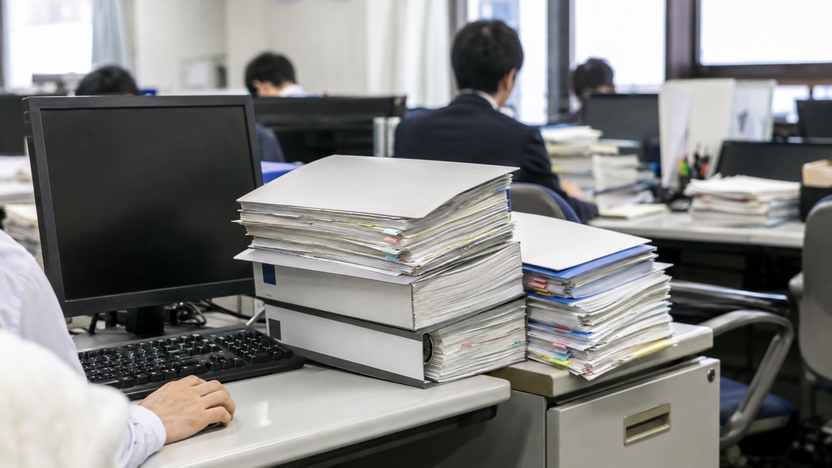 自治体DXでつまずきやすい業務の書類が積まれた執務机